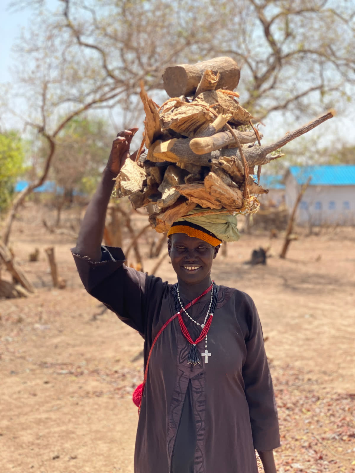 Une femme souriante portant un fagot de bois de chauffage sur la tête dans un village