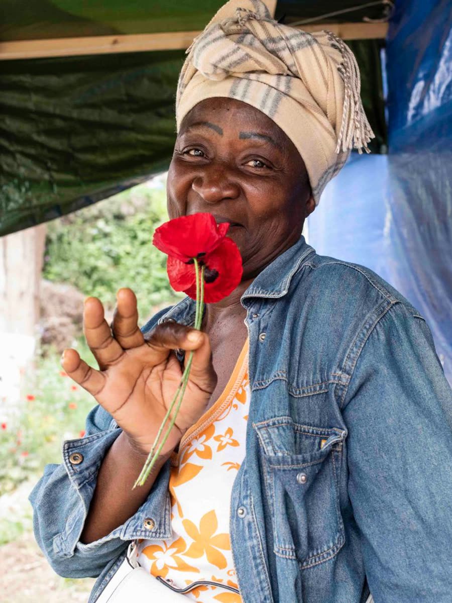 Une femme souriante tenant un coquelicot rouge près de son visage