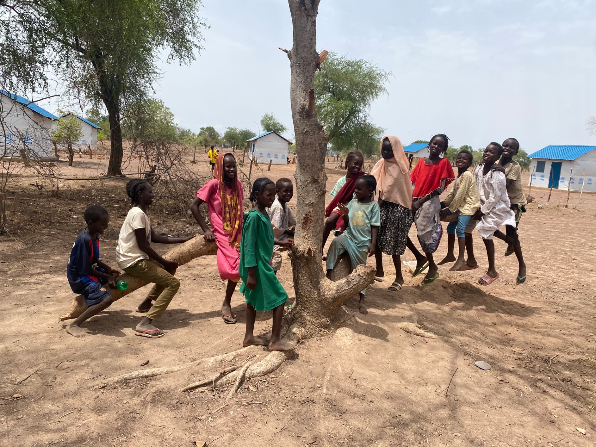 Des enfants d'un camp de réfugiés rassemblés en souriant autour d'un arbre
