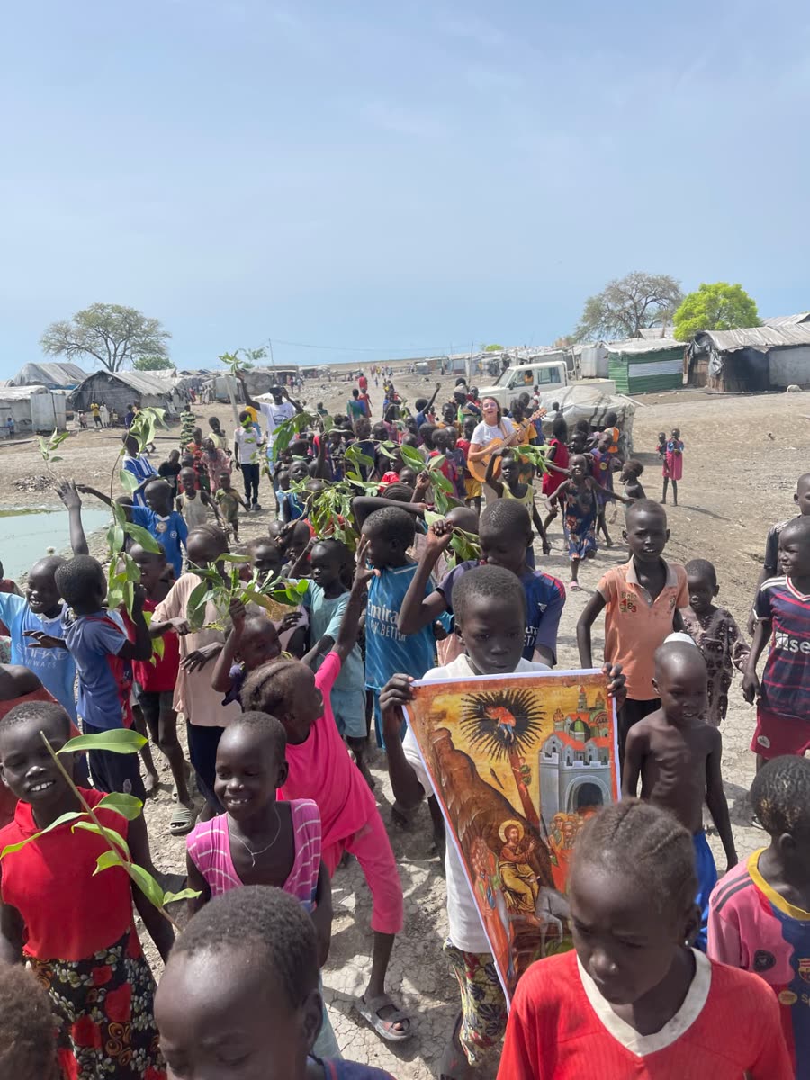Une foule d'enfants en procession avec des rameaux et une icône dans un camp