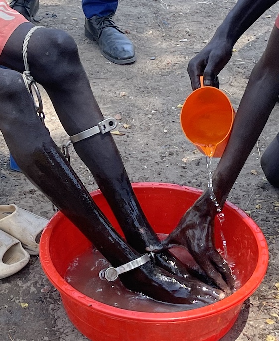 Des mains lavent les pieds enchaînés d'un prisonnier dans une bassine rouge